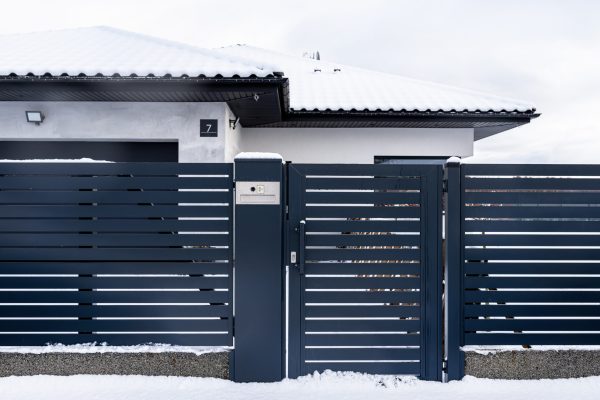 A modern gate with a letterbox and a wireless card reader, mounted in an anthracite panel fence, covered with snow.